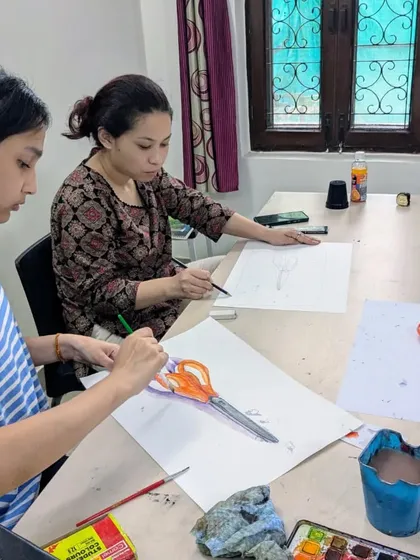 Students concentrating on their object study. One is working on the watercolor version while another refines her pencil sketch of the scissors.