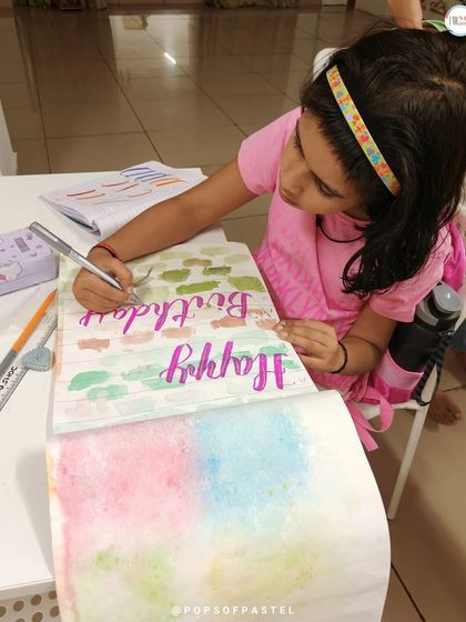 A student works on a "Happy Birthday" card, putting her new brush lettering skills to practical and creative use.