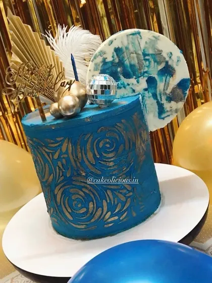 An asymmetrical cake I made for my brother's birthday. This modern design features a bold blue ganache with a gold stenciled pattern, topped with a disco ball, feathers, and an abstract chocolate sail.
