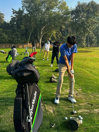 A young golfer in a blue shirt focuses on his setup, with his TaylorMade bag ready for the next shot.