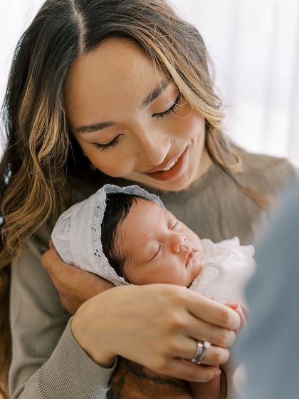 A mother's gentle smile as she holds her sleeping newborn daughter. The soft light and tender expression make this a cherished memory.