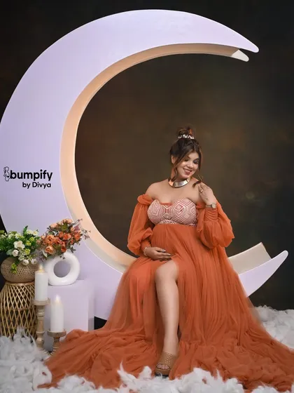 A touch of whimsy and magic in the studio. Here, a glowing mom-to-be is seated on our crescent moon prop, looking like a celestial goddess in a flowing orange gown.