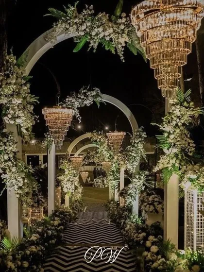 An enchanting floral archway entrance for an evening reception. We used cascading white flowers, crystal chandeliers, and a patterned walkway to create a magical, romantic path for guests.