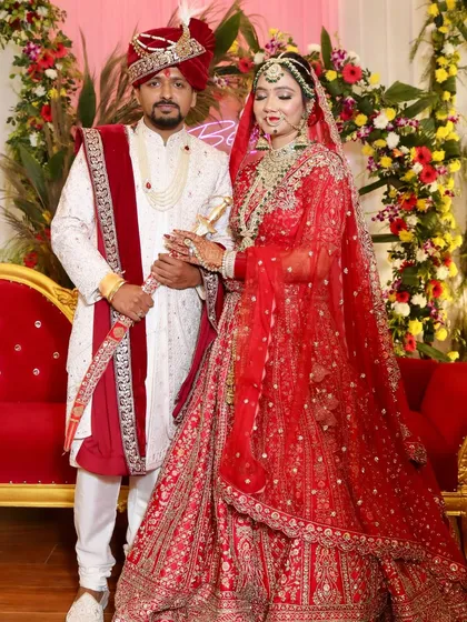A full portrait of the happy couple. Her traditional bridal makeup with a defined eye and red lip stands out beautifully against the festive decor.