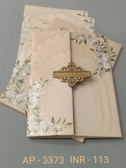 A beautiful gate-fold invitation in a creamy beige, decorated with white lilies and a wooden nameplate. The design is soft, elegant, and comes with three matching inserts.
