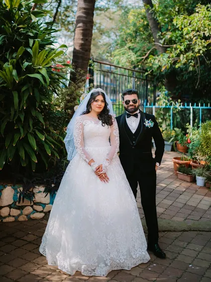A classic, full-length portrait of the bride and groom in their wedding attire, captured in a beautiful garden setting.