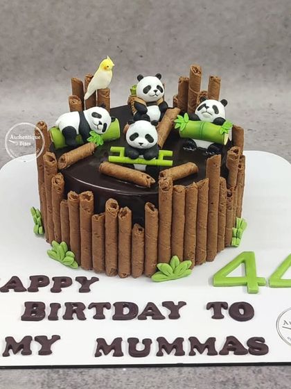 A cute panda cake surrounded by chocolate wafer sticks that look like bamboo.