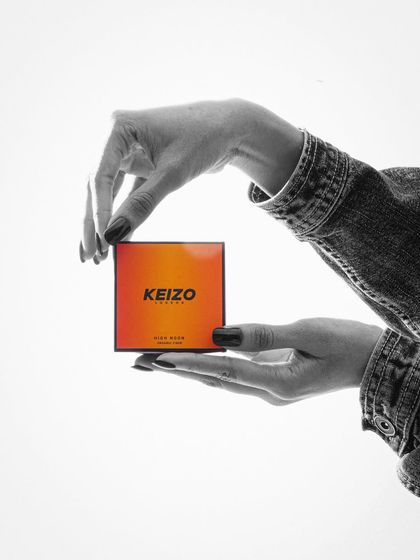 A creative black and white shot with a pop of color, featuring hands framing the "Keizo" product box.