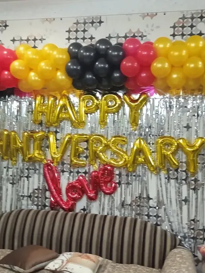 A simple and festive anniversary decoration for your living room. This design uses a silver foil curtain as a backdrop, with 'HAPPY ANNIVERSARY' and 'Love' foil balloons, topped with a colorful balloon garland.