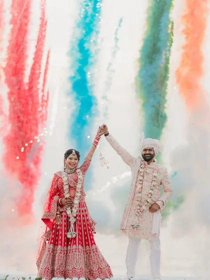A vibrant celebration on the beach. The couple raises their hands in joy as colorful smoke fills the air behind them, creating a spectacular photo.
