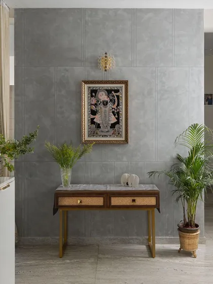 A tranquil corner featuring a traditional Pichwai painting against a modern concrete-finish wall. The simple console table with cane drawers creates a beautiful blend of contemporary design and Indian artistry.