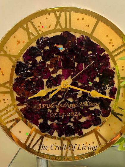 A close-up of a wall clock made with deep purple rose petals. The couple's wedding hashtag and date are included on the clock face, making it a truly personal piece.
