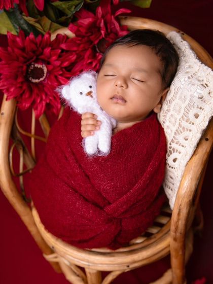 A full view of the maroon-themed setup, with the baby resting in a small rattan chair.