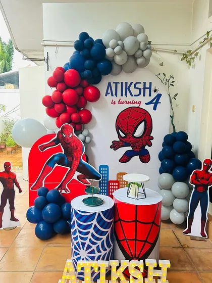 A Spiderman-themed birthday decoration for a 4th birthday party. The setup includes red, blue, and grey balloon arrangements, themed pedestals with web designs, and multiple Spiderman character cutouts.