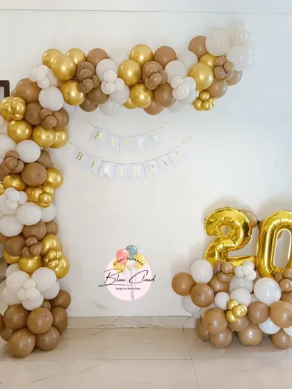 A sophisticated balloon arch in brown, gold, and white for a 20th birthday celebration at home.