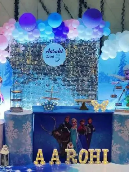 A Frozen party with a large sequin wall as the central backdrop. The setup includes multiple cake stands and character props.