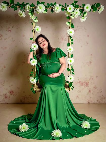 A peaceful portrait of a mom-to-be in a green gown, resting on a swing adorned with white flowers. The textured backdrop adds depth to this studio shot.