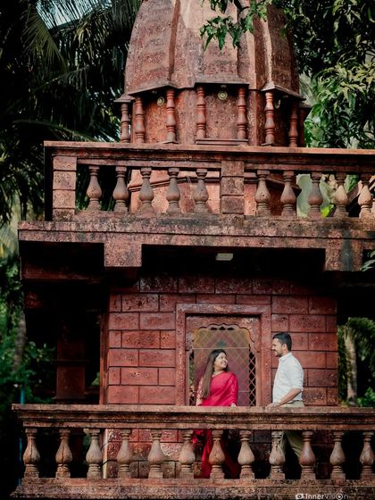 An architectural shot featuring the couple on the balcony of a traditional temple structure. This wide view captures both the grandeur of the location and their presence within it.