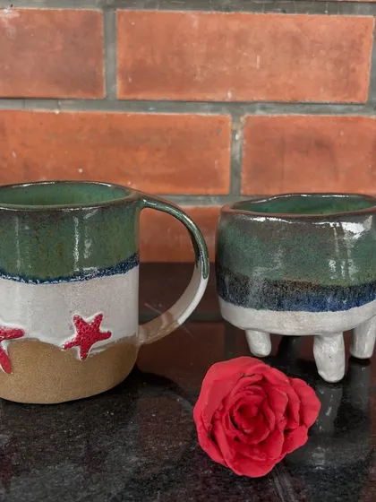 A closer look at two pieces from a young artist's collection: a sea-themed mug with starfish and a small, three-legged planter, both beautifully glazed.