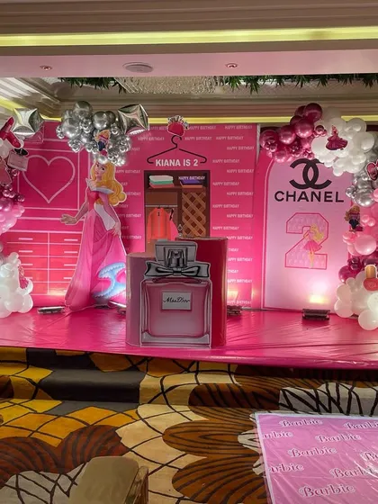 We brought a little girl's fashion-themed dream to life with this vibrant pink stage for her second birthday. The backdrop includes custom elements like a Chanel logo, a princess cutout, and perfume bottle props, making it a perfect photo opportunity.