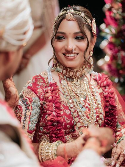 A candid moment of love and laughter during the wedding ceremony. The bride's radiant makeup, with soft waves in her hair, looks stunning with her intricately embroidered red lehenga.