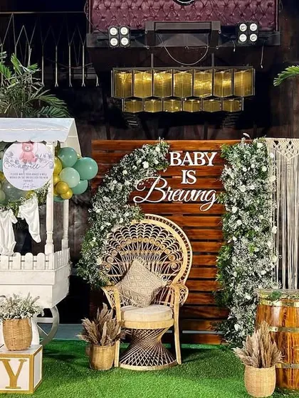 This boho-themed baby shower, with the sign 'Baby is Brewing', combines rustic and chic elements. We used a macrame backdrop, a peacock wicker chair, dried pampas grass, and sage green balloons to create a warm, earthy, and stylish celebration.