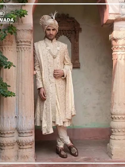 A groom stands amidst ancient pillars, his sherwani a modern tribute to a royal past. The feather in the safa adds a final touch of regal flair.
