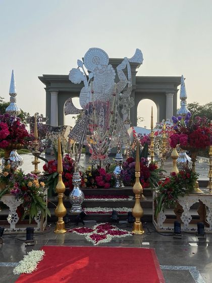 A majestic Shreenathji mandap setup at Raffles Udaipur, designed with opulent red and golden accents. The central idol is flanked by vibrant floral arrangements and traditional golden decor pieces, creating a truly regal and divine atmosphere for the ceremony.