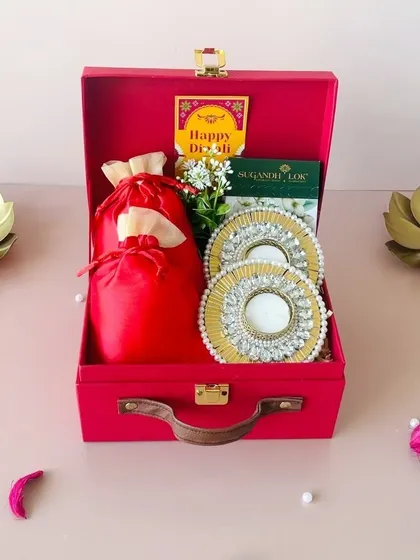 This vibrant red suitcase hamper is a festive delight. It’s packed with stunning pearl and kundan work T-light holders, a satin potli for treats, and a box of incense sticks.
