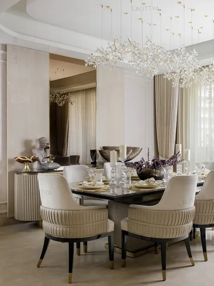 A dining space that speaks through quiet consideration. The table is set for an elegant meal, with pleated-back chairs in a neutral fabric and a stunning crystal chandelier that blooms overhead.