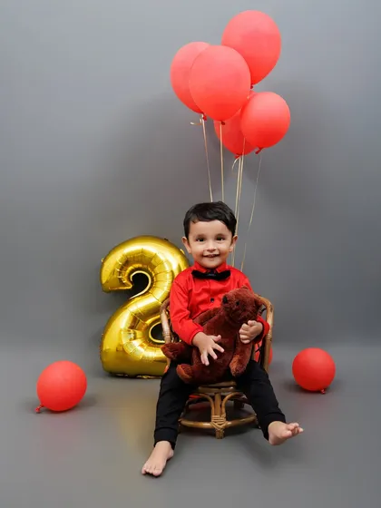 Two cute to handle! A stylish toddler celebrates his second birthday with red balloons and a teddy bear.