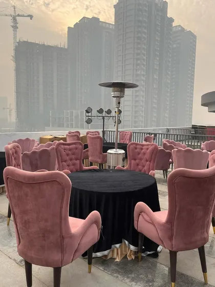 A chic rooftop setup for a cocktail party, featuring modern pink shell-shaped chairs and outdoor heaters for guest comfort.