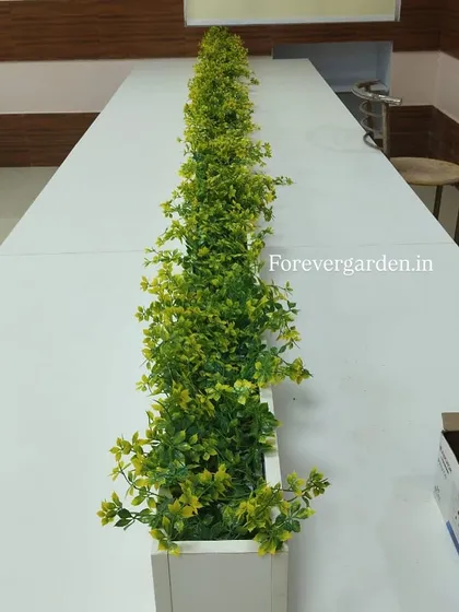 A narrow planter designed to sit on a desk or partition, filled with bright green artificial foliage to bring life to the workspace.