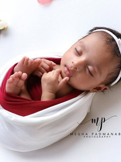 A close-up of a sleeping baby girl in a white wrap and headband, showcasing her beautiful, serene features.