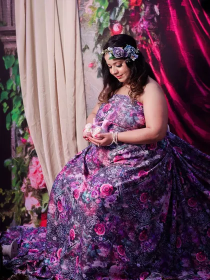 A tender moment captured during a fantasy-themed shoot. The mom-to-be, dressed in a floral gown, cradles a pair of tiny baby shoes, lost in a moment of quiet reflection.
