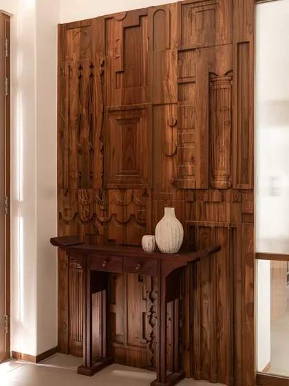 This stunning wall panel is a collage of reclaimed wooden frames and architectural fragments, creating a rich, textured backdrop. In front of it sits a console table with intricately carved legs, celebrating the beauty of handcrafted wood.