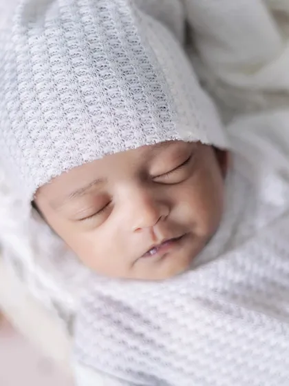 A close-up portrait of a newborn in a simple white wrap and hat. Sometimes, the simplest setups are the most beautiful.