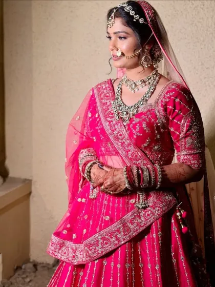 A side profile of a bride in her pink wedding attire, showing the full glory of her embroidered lehenga and dupatta.