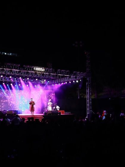 This wide angle shows the full scale of the outdoor stage production for the 'Aai Gavdevi' song release. The powerful lighting rig illuminates the entire performance area, creating a concert-like experience for the audience.