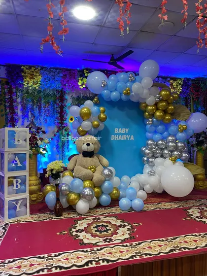 A close-up of the stage decor, highlighting the cute teddy bear nestled within the balloon arch and the 'BABY' blocks on the side.