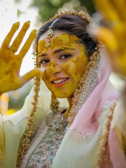 The bride playfully reaches towards the camera with her haldi-covered hands, a fun and engaging shot.