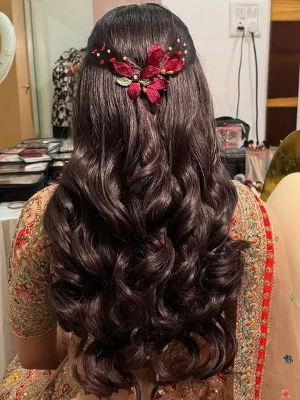 The back of this engagement hairstyle. The soft waves are gathered in a simple half-up style, adorned with a beautiful red floral accessory.