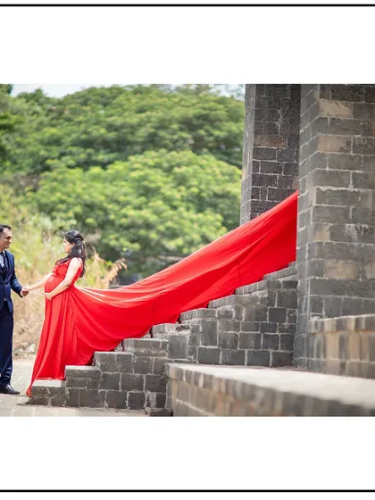 The dad-to-be holds his partner's hand as they stand on a stone staircase, the red gown trailing elegantly behind them.