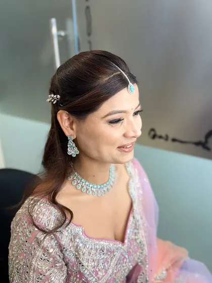 A side profile of the engagement look, showing the elegant hairstyle with a simple hair accessory and the soft, blended eye makeup. The turquoise maang tikka adds a beautiful pop of color.