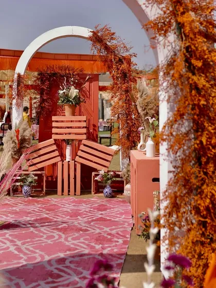 A creative photo-op corner with stacked orange crates and arches, decorated with rustic dried florals, adding an artistic touch to the Haldi event.