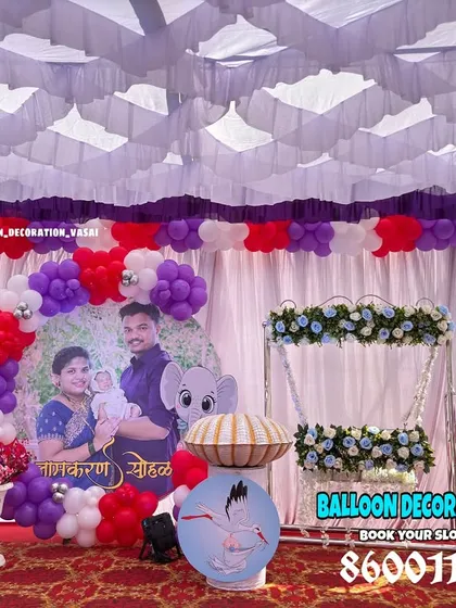 A personalized naming ceremony decoration for an outdoor event. This setup includes a custom photo backdrop of the family, balloon arches, and a beautifully decorated floral jhula for the baby.