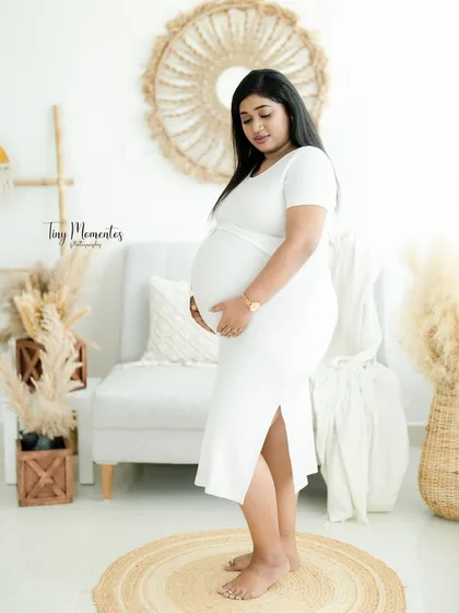 This side profile shot in a simple white dress beautifully showcases the curve of the baby bump against the natural, textured backdrop.