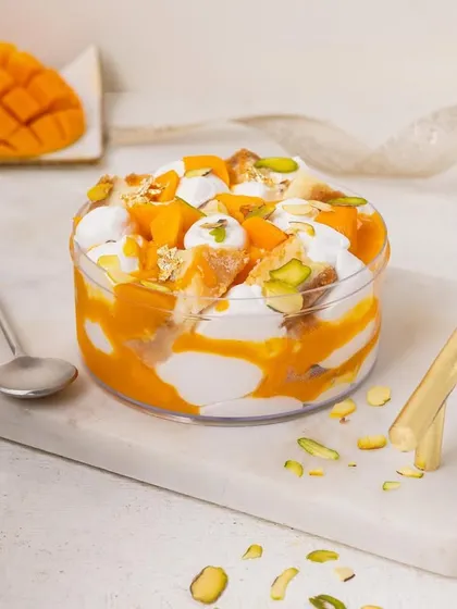 A mango dessert tub with layers of cream and cake, topped with nuts. The composition is clean and focuses on the delicious layers within the tub.