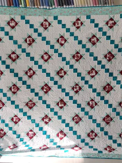 A star quilt with a diagonal setting, combining red floral and teal blocks.