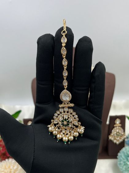 The Ziva Premium Moissanite Kundan Necklace. This choker set is defined by its floral-inspired motifs, pearl droppings, and a matching maang tikka, available in both red and green stone options.